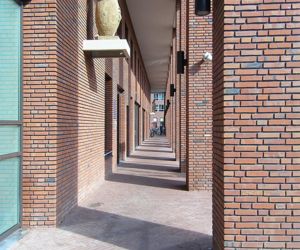 Eine perspektivische Aufnahme des Säulengangs eines Wohngebäudes. Die Wände und Säulen sind mit typischer niederländischer Backsteinfassade erbaut. Der Boden des Säulengangs wurde mit Brandziegeln in etwas dunkleren Farbe gepflastert.